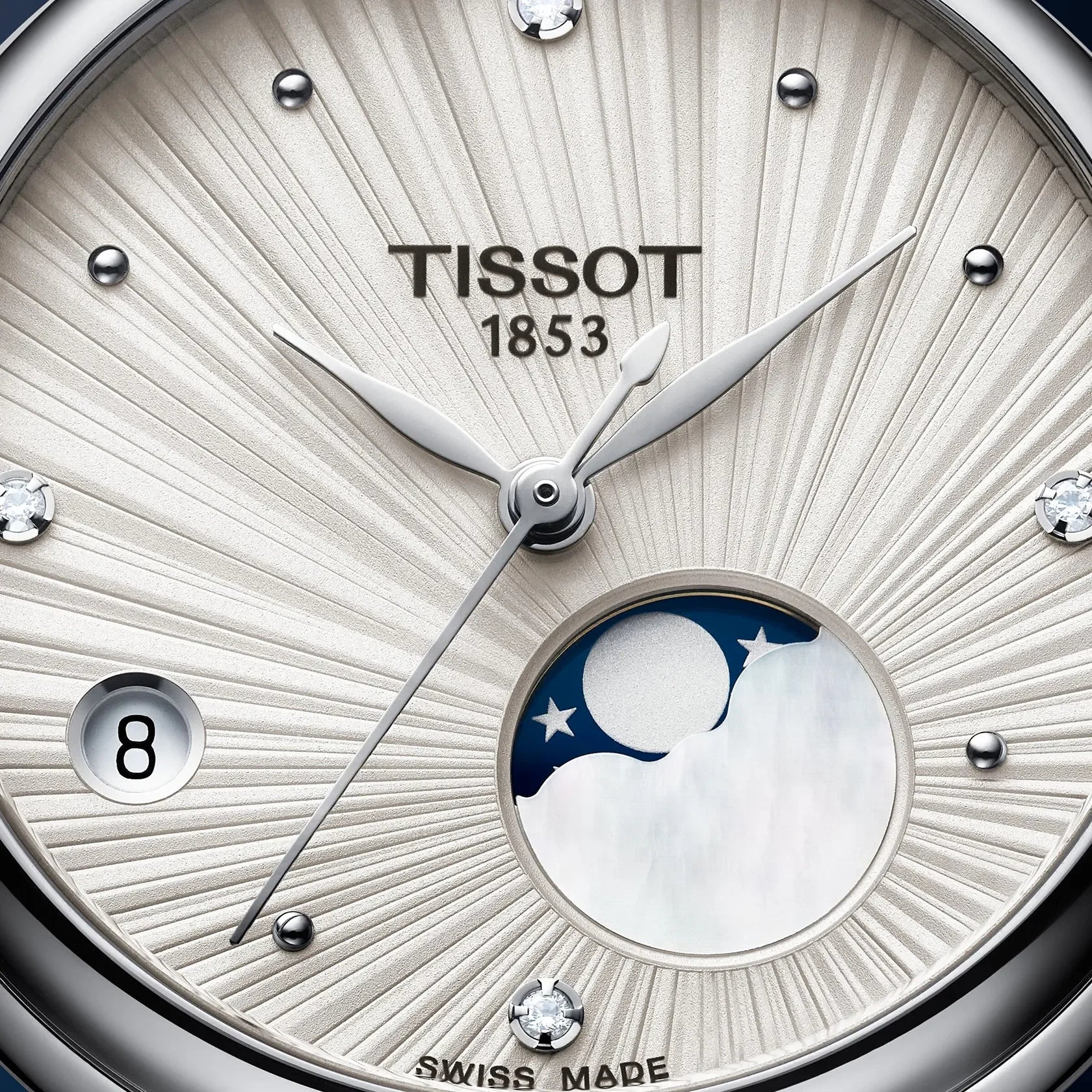 Close-up of a Tissot 1853 watch dial featuring a sunburst silver and white textured face, a moonphase indicator with a blue and white night sky motif, and crystal hour markers.