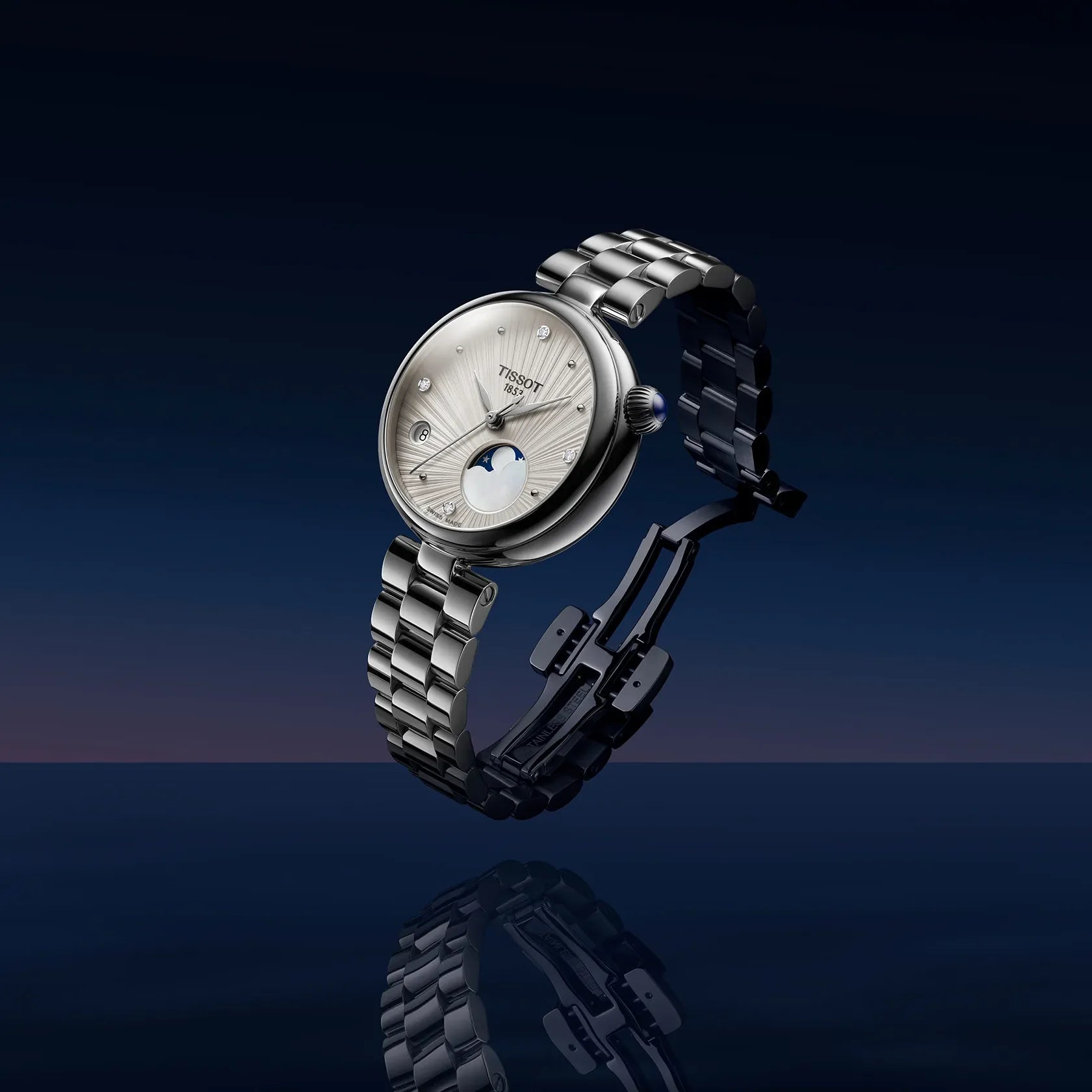 A Tissot women's watch with a silver stainless steel bracelet and a white dial featuring a moonphase indicator, shown floating against a dark blue gradient background with a reflection below.