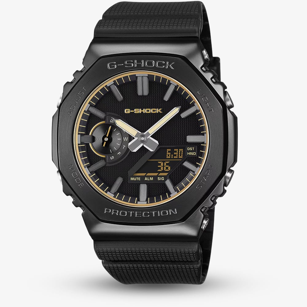 A black G-Shock analog watch with a textured black strap, black case, and gold-tone accents on the dial, shown against a light gray background.