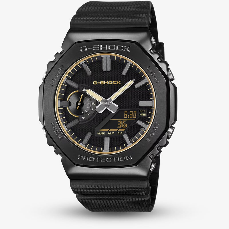 A black G-Shock analog watch with a textured black strap, black case, and gold-tone accents on the dial, shown against a light gray background.