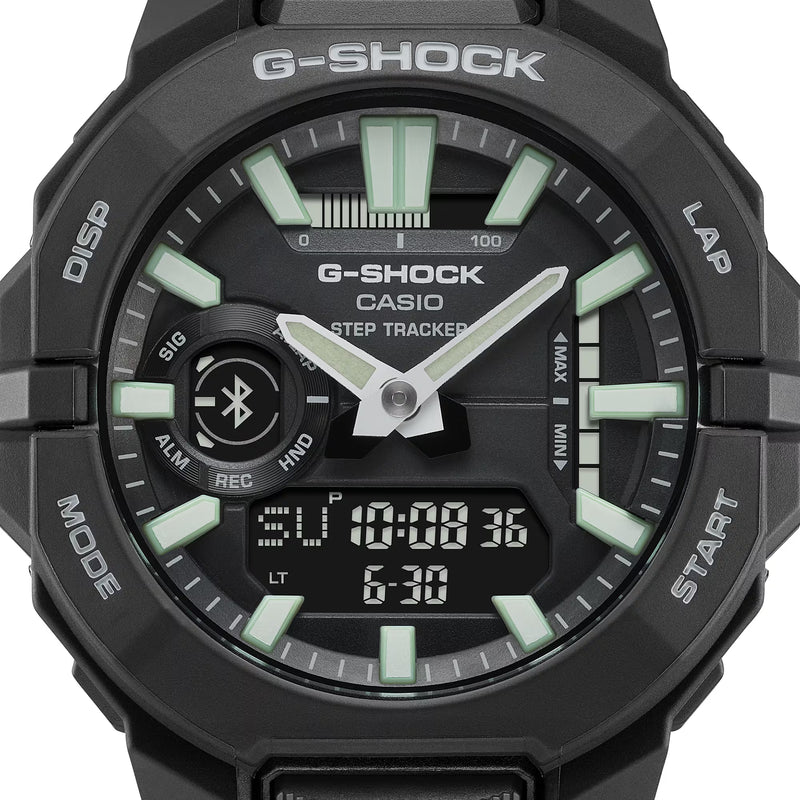Close-up of a black Casio G-SHOCK ana-digi watch face featuring green luminous hour markers, silver hands, Bluetooth symbol, step tracker and digital display.